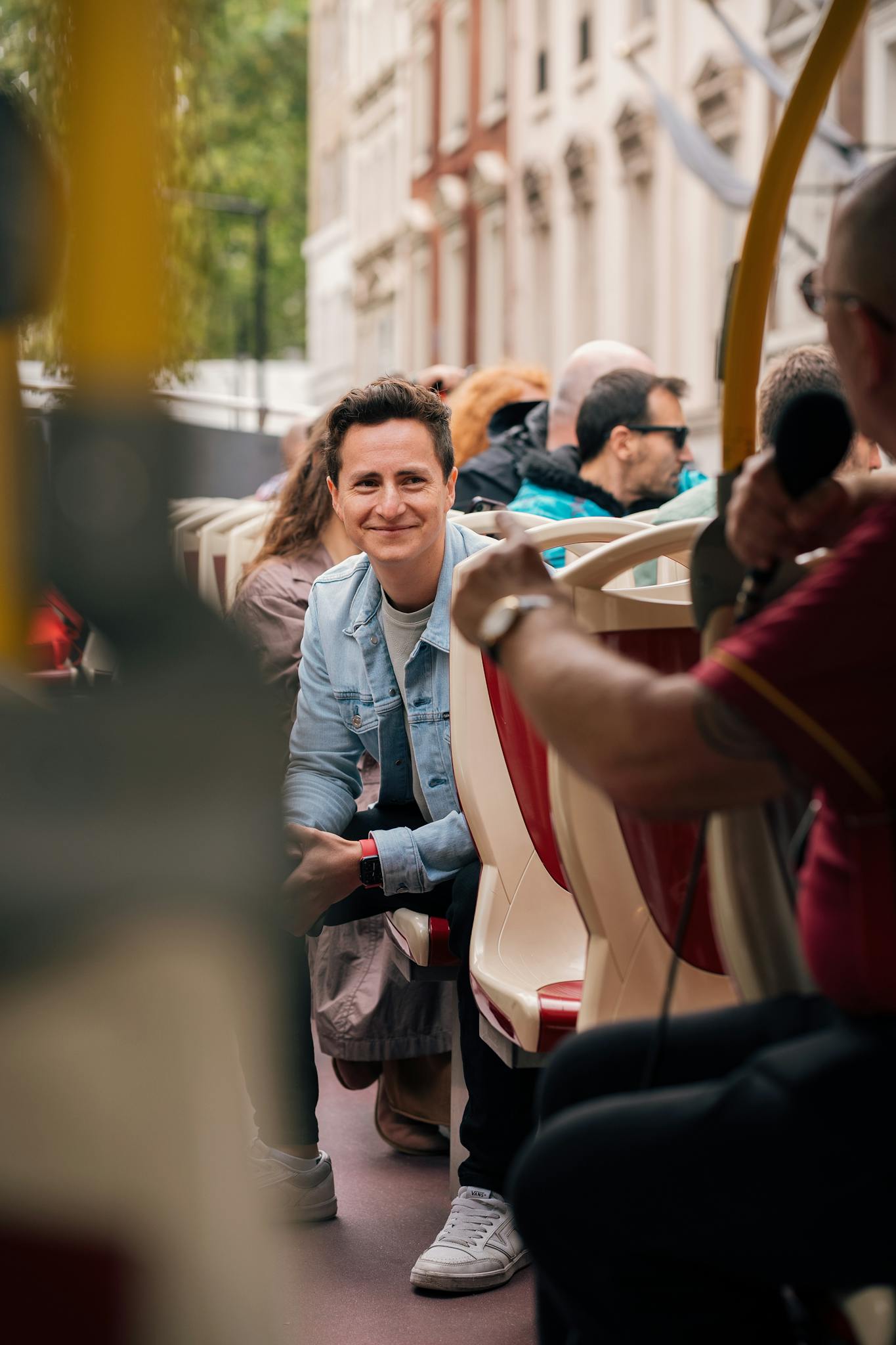 A smiling man enjoys a guided open-top bus tour in the city.